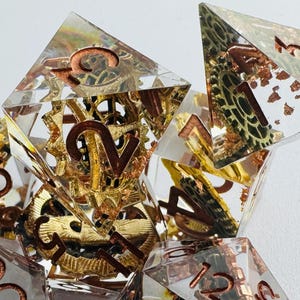 May include: Set of seven polyhedral dice with a steampunk theme. The dice are clear with copper-colored numbers and embedded with gears and other mechanical elements in gold and copper. The dice are arranged on a white surface.