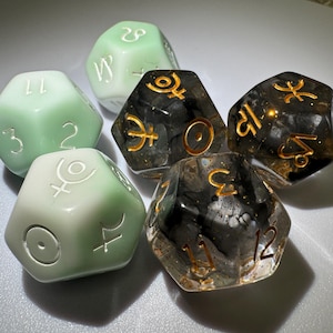 May include: Six polyhedral dice in shades of green and black. The dice feature gold-colored numbers and symbols. Some dice are translucent, revealing internal patterns. The dice are designed for tabletop gaming.