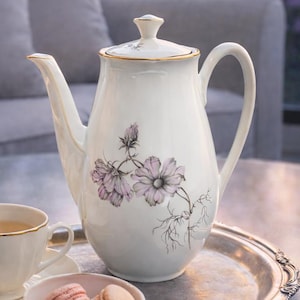 May include: A white ceramic mug with a black handle and the text "But First, Coffee" in a bold, black font. The mug is set against a neutral background, highlighting its simple design.