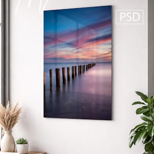 Puede incluir: Una maqueta metálica enmarcada que presenta un sereno paisaje marino con postes de madera que se extienden hacia el agua. El cielo muestra una vibrante puesta de sol con tonos de azul, rosa y naranja. Las palabras "Metal Mockup" y "PSD" son visibles.