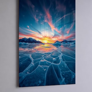 May include: A framed print depicting a scenic landscape. The image showcases a cracked, icy surface in the foreground, leading to a mountain range under a vibrant sunset sky with orange and blue hues. The artwork is mounted on a white wall.