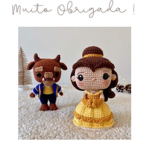Puede incluir: Muñecos de ganchillo de Bella y la Bestia de La Bella y la Bestia. Bella lleva un vestido amarillo, y la Bestia tiene una chaqueta azul. El texto "Muito Obrigada !" está escrito en cursiva en la parte superior de la imagen.