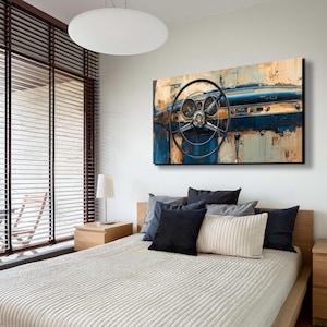 May include: An abstract painting of a classic car dashboard and steering wheel. The artwork features a colour palette of blue, brown, and beige, with visible gauges and a detailed steering wheel. The painting is mounted above a bed with pillows.