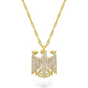 Puede incluir: Un collar dorado con un colgante en forma de águila. El colgante de águila está incrustado con pequeñas piedras preciosas transparentes. La cadena tiene un diseño de cuerda trenzada. El collar se muestra sobre un fondo blanco.