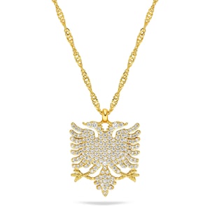 Puede incluir: Un collar dorado con un colgante en forma de águila bicéfala, incrustado con numerosas piedras preciosas pequeñas y transparentes. La cadena tiene un diseño de cuerda trenzada. El colgante mide aproximadamente 3,8 cm de ancho y 4,4 cm de alto.