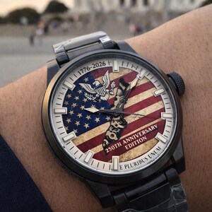 K&ouml;nnte beinhalten: Schwarze Armbanduhr mit patriotischem Design. Das Zifferblatt zeigt die amerikanische Flagge, einen Adler und den Text "1776-2026 250th Anniversary Edition E Pluribus Unum." Die Uhr hat ein schwarzes Metallarmband.
