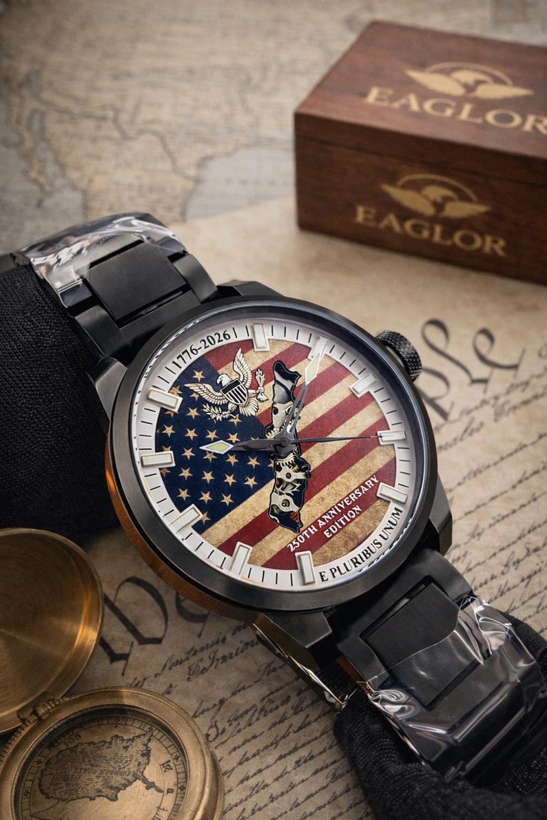 K&ouml;nnte beinhalten: Schwarze Armbanduhr mit patriotischem Design. Das Zifferblatt zeigt die amerikanische Flagge, ein Adleremblem und den Text "1776-2026" und "250th Anniversary Edition". Die Uhr wird mit einer Holzbox pr&auml;sentiert.