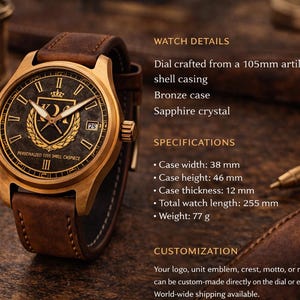 May include: A bronze wristwatch with a brown leather strap. The watch face is dark with gold detailing, including a crest and Roman numerals. The case width is 3.8 cm, and the total watch length is 25.5 cm.