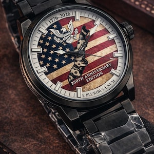 K&ouml;nnte beinhalten: Schwarze Armbanduhr mit patriotischem Design. Das Zifferblatt zeigt die amerikanische Flagge, ein Adleremblem und den Text "1776-2026" und "250th Anniversary Edition". Die Uhr hat ein schwarzes Metallarmband.
