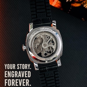 Puede incluir: Un reloj de pulsera plateado con correa negra texturizada y movimiento mec&aacute;nico a la vista. La parte posterior de la caja de metal presenta el texto grabado "To my Amar, I love you" y "Maria". El reloj se muestra junto al texto "YOUR STORY. ENGRAVED FOREVER. ANY TEXT. ANY IDEA. MADE JUST FOR YOU."