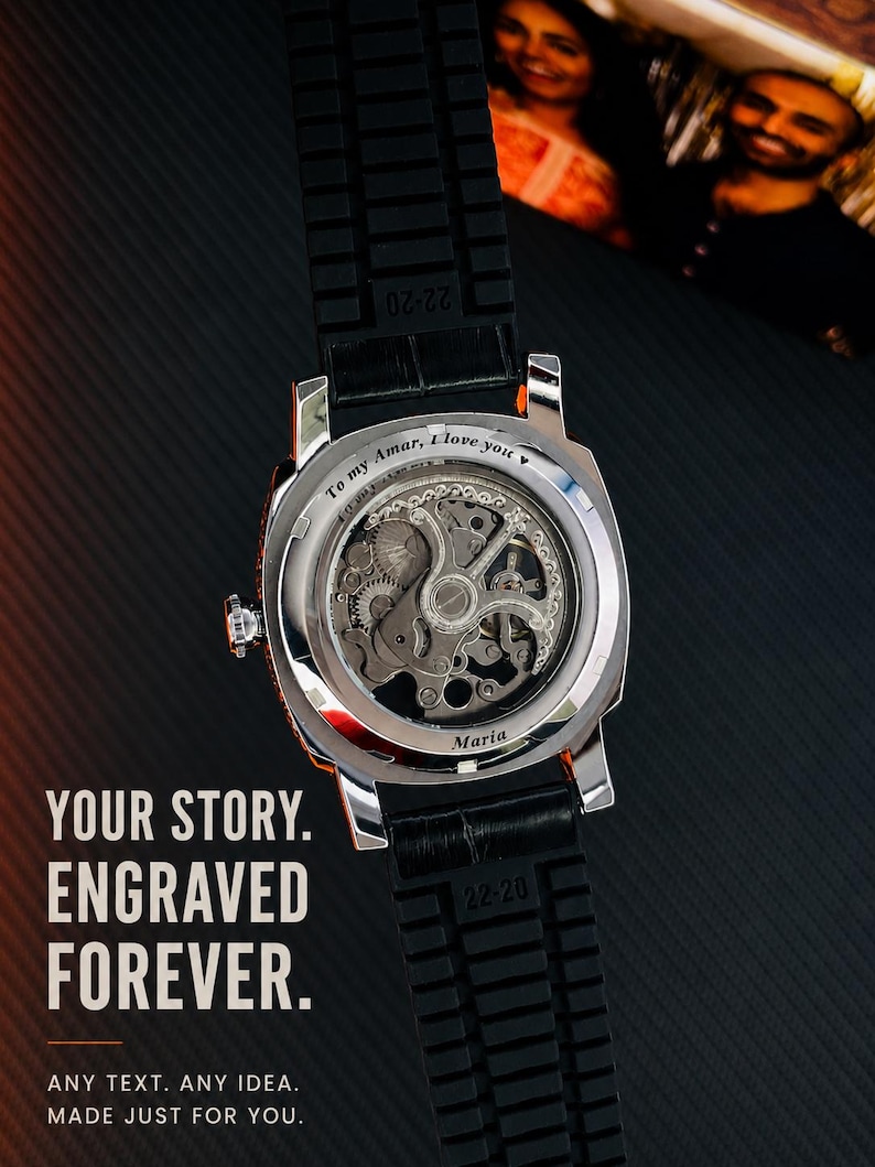 Puede incluir: Un reloj de pulsera plateado con correa negra texturizada y movimiento mec&aacute;nico a la vista. La parte posterior de la caja de metal presenta el texto grabado "To my Amar, I love you" y "Maria". El reloj se muestra junto al texto "YOUR STORY. ENGRAVED FOREVER. ANY TEXT. ANY IDEA. MADE JUST FOR YOU."
