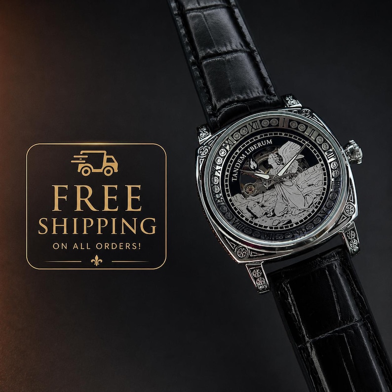 Puede incluir: Un reloj de pulsera plateado con correa de cuero negro con textura de cocodrilo. La esfera muestra una ilustraci&oacute;n detallada de un &aacute;ngel, el texto TANDEM LIBERUM y n&uacute;meros romanos a lo largo del borde del bisel circular.