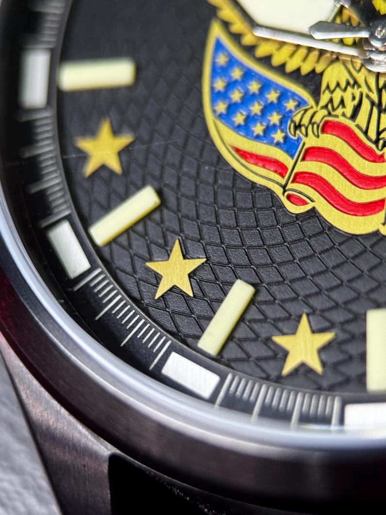 K&ouml;nnte beinhalten: Nahaufnahme eines Armbanduhr-Zifferblatts mit schwarzem strukturiertem Hintergrund. Das Zifferblatt zeigt goldene Sterne, ein gelb-rotes Flaggenmuster und ein silbernes Uhrengeh&auml;use. Die Zeiger der Uhr sind sichtbar.