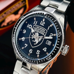 Op de afbeelding: Een roestvrijstalen polshorloge met een donkerblauwe wijzerplaat. Het horloge heeft een datumweergave en een gedetailleerde wijzerplaat met witte cijfers en wijzers. De horlogeband is ook van roestvrij staal. De wijzerplaat bevat tekst in een vreemde taal.