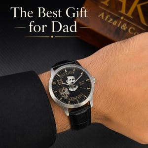 May include: A silver-tone wristwatch with a black dial featuring a portrait, the text MUXSIN, Afzal & Co, and for my father, with a black leather strap. The text The Best Gift for Dad is visible above, and a wooden box with AK Afzal & Co is nearby.