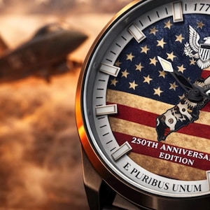 K&ouml;nnte beinhalten: Eine Armbanduhr mit einem dunklen Metallarmband und einem Zifferblatt mit dem Design der amerikanischen Flagge. Das Zifferblatt enth&auml;lt den Text "250th Anniversary Edition" und "E Pluribus Unum". Der Hintergrund zeigt ein verschwommenes Bild eines Jets.