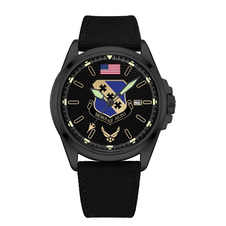 May include: Black wristwatch with a textured face featuring the American flag and a military emblem. The watch has a black band and a date display at the 3 o'clock position. The watch face also includes the text "MORS AB ALTO".