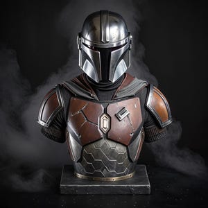 May include: A detailed bust of The Mandalorian, featuring a silver helmet and weathered brown and silver armor. The bust is set against a dark background, showcasing the intricate details of the costume.