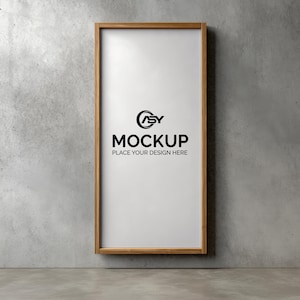 May include: A rectangular wooden frame with a white interior, hanging on a gray concrete wall. The frame contains the word "MOCKUP" in bold black letters, with the text "PLACE YOUR DESIGN HERE" below it. A logo is above the word "MOCKUP".
