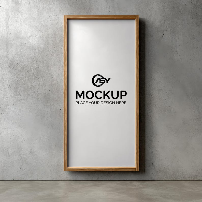 May include: A rectangular wooden frame with a white interior, hanging on a gray concrete wall. The frame contains the word "MOCKUP" in bold black letters, with the text "PLACE YOUR DESIGN HERE" below it. A logo is above the word "MOCKUP".
