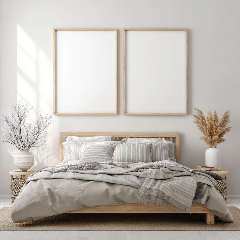 May include: A cozy bedroom scene featuring a wooden bed frame with neutral-toned bedding and pillows. Two framed blank art prints hang above the bed. Decorative elements include vases with dried plants and woven side tables, creating a serene, minimalist aesthetic.