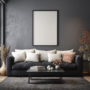 May include: A modern living room with a dark gray sofa, adorned with cream-colored pillows and a patterned orange cushion. A black framed blank canvas hangs above the sofa. A dark gray rug and coffee table complete the scene.
