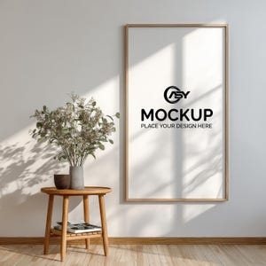May include: A wooden framed mockup poster with the text "MOCKUP PLACE YOUR DESIGN HERE" is displayed on a white wall. A small wooden side table holds a vase of flowers and a small bowl. The room has a natural, minimalist aesthetic.