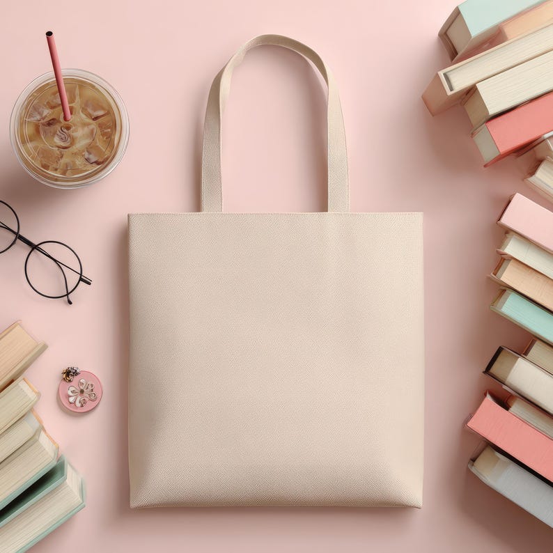 May include: A beige tote bag with handles, a clear iced coffee with a pink straw, a pair of round black glasses, a pink floral pin, and several stacks of books are arranged on a pink background.