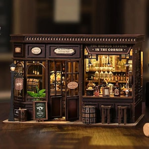 Può includere: Modello in miniatura di una taverna in legno con il testo "TASTY" e "THE HIDDEN TAVERN IN THE CORNER." Il modello presenta un bar, bottiglie e un'insegna "WINE SHOP". Il modello è marrone con illuminazione interna.