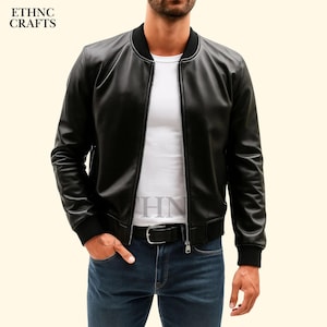 May include: A black leather bomber jacket with a zip-up front, black ribbed cuffs, and a black ribbed hem. The jacket has a black collar and a white lining. The model is wearing blue jeans and a black belt. The text "ETHNC CRAFTS" is visible.
