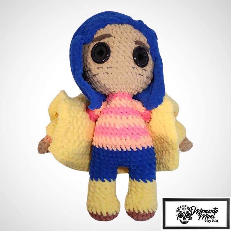 May include: A handmade crochet doll with blue hair, large black button eyes, and a tan face. The doll wears a pink and orange striped shirt, blue pants, and yellow boots. A yellow jacket is draped over the doll's shoulders. The doll is a character from a movie.