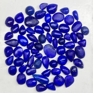 May include: A collection of polished lapis lazuli gemstones in various shapes, including teardrops, ovals, and irregular forms. The stones display a deep, rich blue color with subtle variations and flecks of gold. The gemstones are arranged closely together.