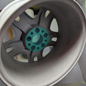 Op de afbeelding: Een close-up van een grijze velg met een turquoise middennaaf. De velg heeft een multi-spaaks ontwerp en een afgeronde buitenrand. Het wiel lijkt nieuw en schoon te zijn.