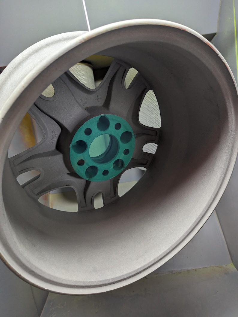 Op de afbeelding: Een close-up van een grijze velg met een turquoise middennaaf. De velg heeft een multi-spaaks ontwerp en een afgeronde buitenrand. Het wiel lijkt nieuw en schoon te zijn.