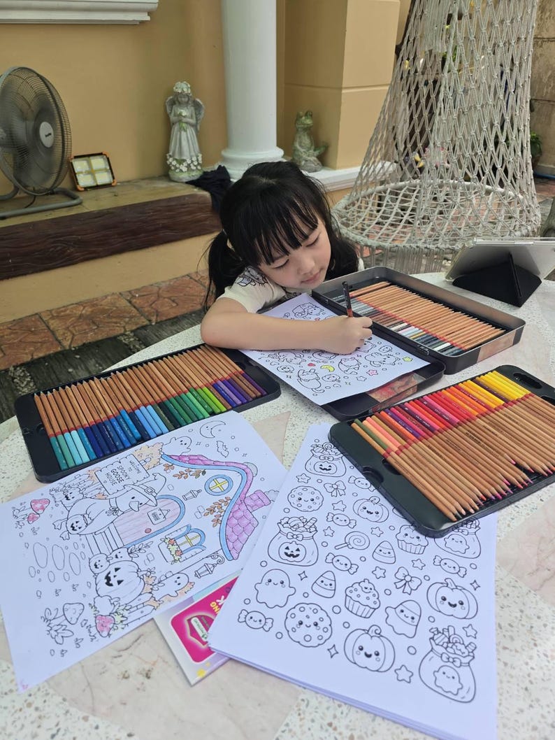 Pu&ograve; includere: Tre scatole metalliche rettangolari riempite con matite colorate assortite disposte in file, che circondano diversi fogli di carta bianca con illustrazioni a linee in bianco e nero di zucche, fantasmi e caramelle da colorare.