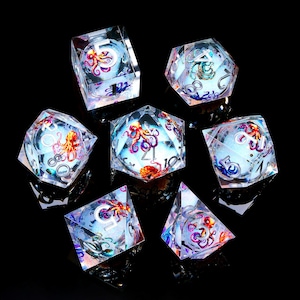 May include: A set of seven clear, multi-sided dice with an octopus design inside. The dice have a shimmering, iridescent effect with red, orange, and purple octopus illustrations. The numbers are in silver. The dice are for tabletop games.