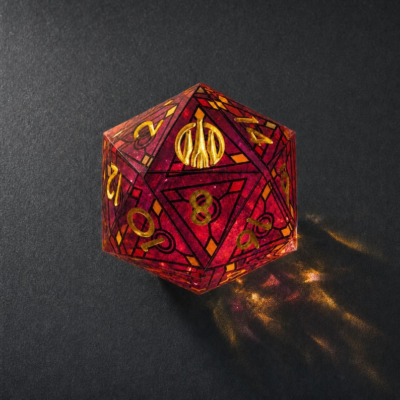 May include: A twenty-sided die featuring a deep red, translucent resin body with an intricate stained-glass style pattern in black and gold. The numbers are etched in gold, and a golden emblem of three vertical pillars replaces the number twenty.