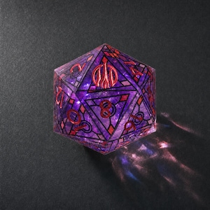 May include: A twenty-sided die featuring a translucent purple and blue galaxy-like interior. The surface is decorated with black geometric stained-glass style lines and red numbering. A red trident symbol replaces the number twenty on the top face.