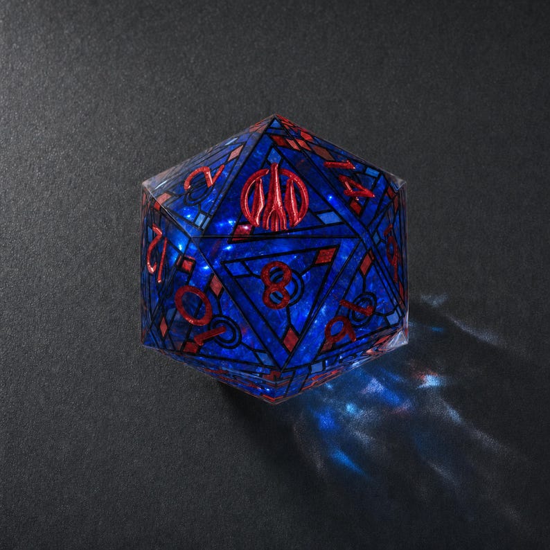 May include: A twenty-sided die featuring a deep blue translucent body with a stained glass-like pattern of dark blue lines. The numbers and a central emblem are embossed in a metallic red finish, creating a sharp contrast against the blue.