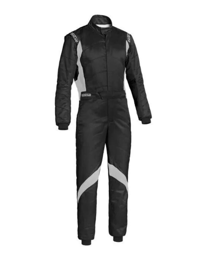 May include: Black racing suit with white accents. The suit has a high collar, long sleeves, and a full-length zipper. The Sparco logo is visible on the shoulders and chest. The suit is designed for motorsports.