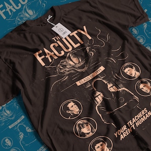 May include: Dark brown t-shirt with a graphic design featuring the text "THE FACULTY" and "CLASS OF 1999". The design includes a monster illustration and several circular portraits. The phrase "YOUR TEACHERS AREN'T HUMAN" is also visible.