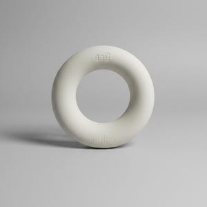May include: A light grey, circular hand grip exerciser with a smooth, matte finish. The text 5LB is embossed on the top section, and the brand name Kallpa is embossed on the bottom section of the ring, which is designed for strength training.