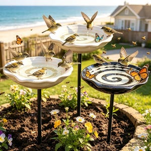 Könnte beinhalten: Ein Set aus drei Vogeltränken auf schwarzen Metallständern, bestehend aus zwei weißen, gewellten Becken und einem schwarz-weiß spiralförmig gemusterten Becken, umgeben von kleinen Vögeln, Monarchfaltern und Bienen im Garten.