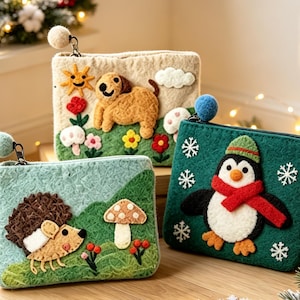 Könnte beinhalten: Drei rechteckige Reißverschlusstaschen aus Filz mit Nadelfilz-Applikationen. Eine cremefarbene Tasche zeigt einen braunen Hund, Sonne und Blumen. Eine hellgrüne Tasche zeigt einen braunen Igel und einen Pilz. Eine dunkelgrüne Tasche zeigt einen Pinguin mit rotem Schal.