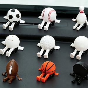 May include: A collection of sports-themed car air fresheners. The set includes a soccer ball, baseball, bowling pin, bowling ball, golf ball, volleyball, football, basketball, and a hockey puck, each with arms and legs.