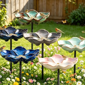Könnte beinhalten: Eine Ansammlung von sechs blumenförmigen Vogelfutterstellen auf schwarzen Metallstäben mit glasierten Keramikschalen in Türkis, Marineblau, Grau, Hellblau und Blassrosa, die mit Vogelfutter gefüllt sind und von kleinen Vögeln besucht werden.