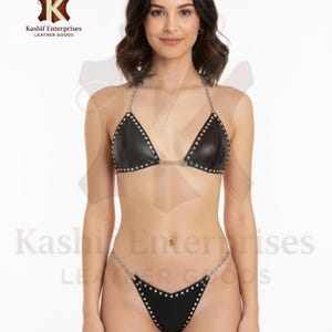 Könnte beinhalten: Schwarzes Leder-Bikini-Set mit silberfarbenen Kettenriemen und Nieten. Das Triangel-Oberteil und der Tanga-Slip sind mit silbernen Nieten besetzt. Der Text "Kashif Enterprises Leather Goods" ist im Bild enthalten.