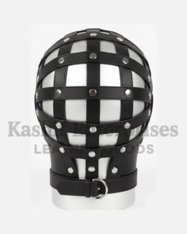 Puede incluir: Un arn&eacute;s de cabeza de cuero negro con un dise&ntilde;o en forma de jaula. El arn&eacute;s presenta correas horizontales y verticales aseguradas con remaches plateados. Una correa con una anilla en D de metal rodea la zona del cuello. El texto "Kas Leather Goods" es visible.