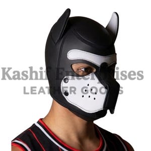 May include: A black and white leather puppy hood with ear details and a muzzle. The hood has a white section around the eyes and mouth, with small ventilation holes. The text "Kashif Enterprises LEATHER GOODS" is visible.