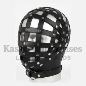 Puede incluir: M&aacute;scara de cabeza de cuero negro con un dise&ntilde;o de jaula. La m&aacute;scara presenta correas horizontales y verticales aseguradas con remaches plateados. Una correa con un anillo de metal est&aacute; alrededor del cuello. El texto "Kas" y "Goods" es visible.